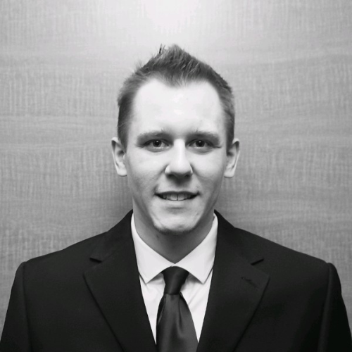 Black-and-white headshot of a man in a suit and tie, facing the camera with a slight smile against a neutral background.