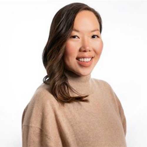 Headshot of a smiling woman wearing a beige sweater against a light gray background.