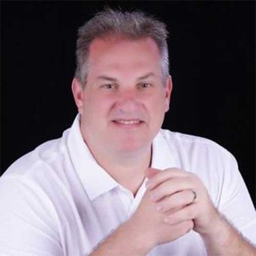Smiling man in a white polo shirt against a black background.