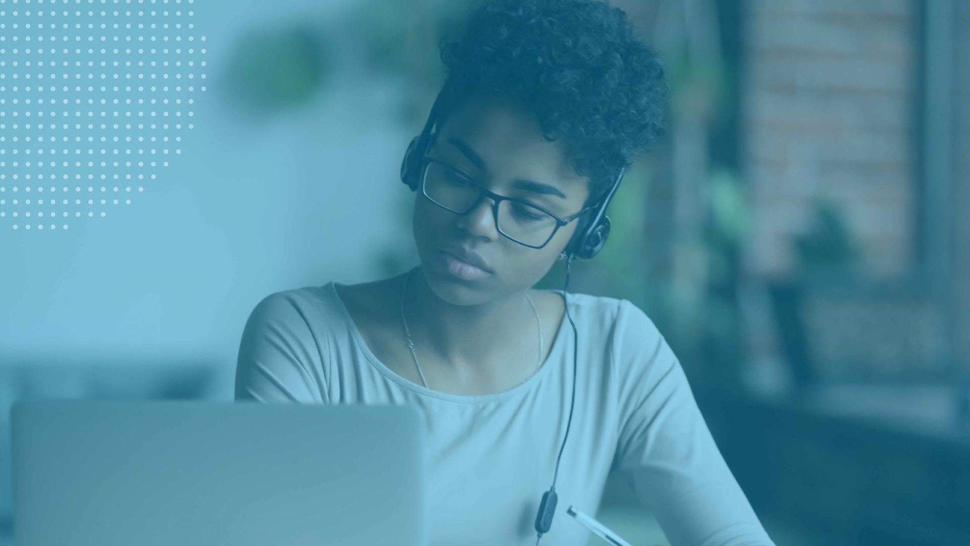 Professional wearing a headset takes notes while attending a webinar on a laptop.